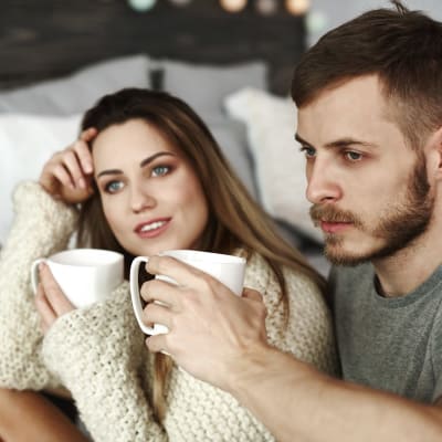 Leende kvinna och fundersam man med kaffemuggar i händerna