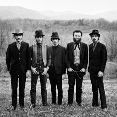 The Band-yhtyeen jäsenet eli viisi miestä seisoo rinnakkain mustavalkoisessa kuvassa, joka on otettu maalaismasemassa. 