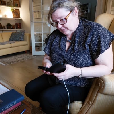 Författaren och historikern Carina Nynäs sitter i sitt hem på Sirkkalagatan i Åbo och studerar sin mobiltelefon som är på laddning.