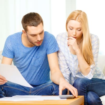 Ung man och kvinna sitter i en soffa och ser på några dokument och en miniräknare