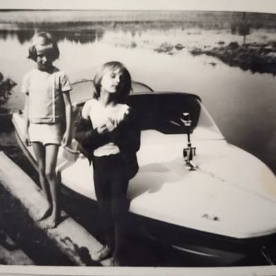 Kaksi tyttöä seisoo pienen moottoriveneen edessä laiturilla. 