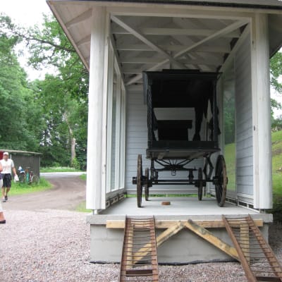 En gammal hästdragen likvagn står i sitt utställningsbås utanför kyrkan i Svartå.