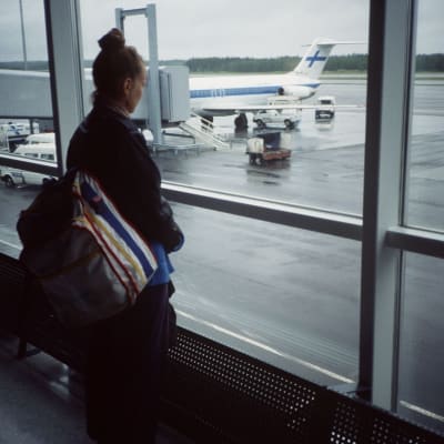 Ung kvinna tittar ut genom fönstret på flygfältets landningsbana.