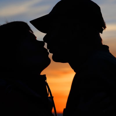 mies ja nainen suutelee auringonlaskussa