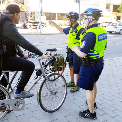 Cyklist på trottoaren stoppas av två poliser. 