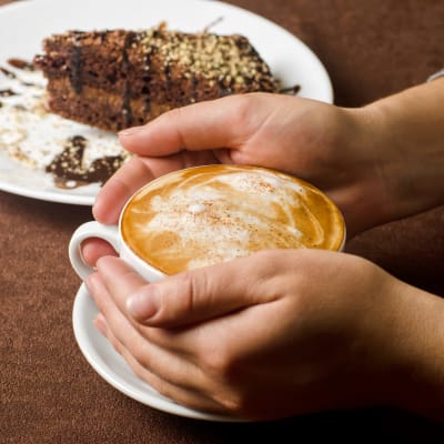 Händer håller om en kopp kaffe (cappucino)
