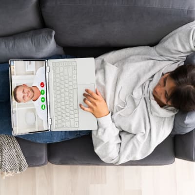 en kvinna ligger i en soffa och har en dator i famnen som hon videochattar med 