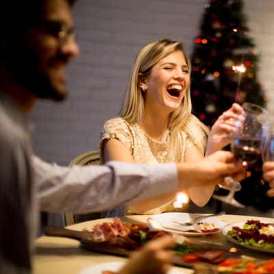 En kvinna skrattar och skålar vid ett julbord med sina vänner.