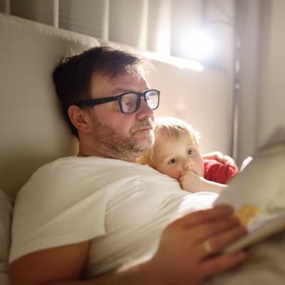 En pappa som läser en godnattsaga för sitt barn i en stor säng.
