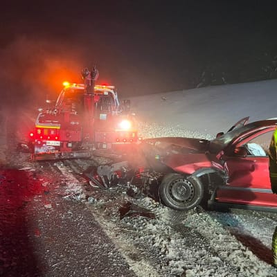 En olycksplats där en röd personbil kört in i en bärgningsbil. På ena sidan står en brandman och inspekterar platsen.