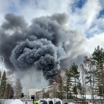Mörka rökmoln stiger upp ur en byggnad. Människor utrymmer området.