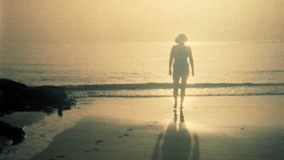 Nainen kävelee hiekkarannalla auringonlaskun aikaan.