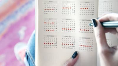 En människa antecknar menstruationscykeln i en kalender med röda prickar.