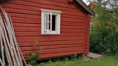 En röd trästuga med öppet fönster.