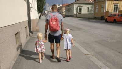 Pappa Nicklas promenerar längs en trottoar med ett barn i var hand.