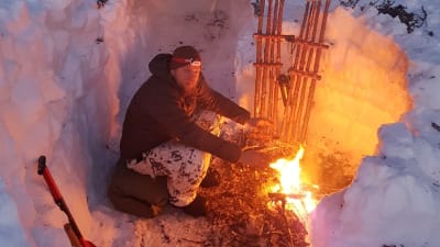 Mies lämmittelemässä nuotiolla.
