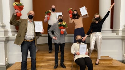 En grupp människor står med prisdiplom och blommor i händerna. 