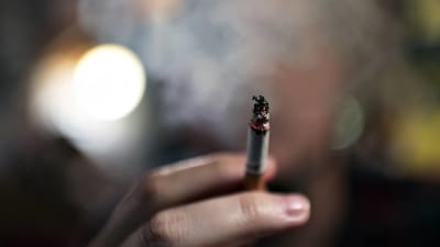 En hand håller i en tänd cigarett. Svart bakgrund. 