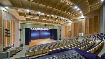 En konsertsal med flera hundra platser. träkonstruktioner, bänkar i trä och blått, belyst scen.