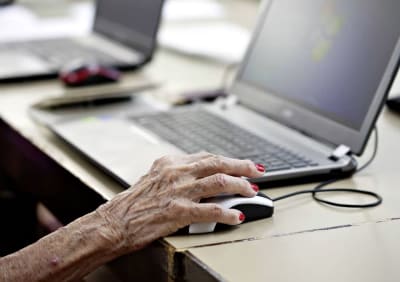 En hand som tillhör en äldre person håller i en datormus.