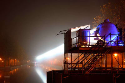 En byggställning med en strålkastare, som står vid en dimmig åstrand.