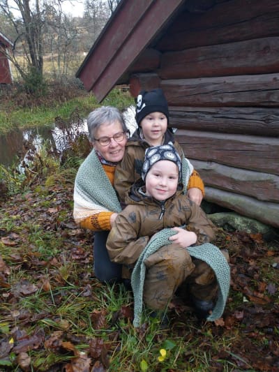 Kvinna med två barn inlindade i en stickad sjal.