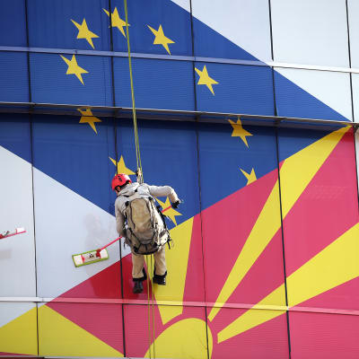 Työntekijät puhdistavat EU:n ja Pohjois-Makedonian lipuilla koristettua ikkunaa.