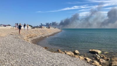Turister på en strand på Krim tittar på en rökpelare som stiger från en flygbas efter flera explosioner.