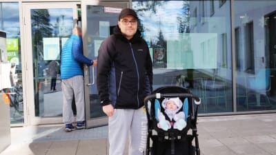 En man står bredvid en barnvagn med ett litet barn i. 