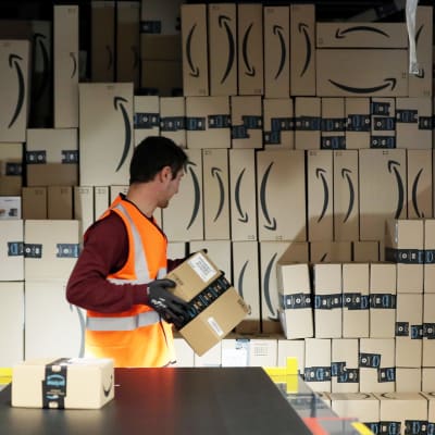 Työntekijä lastaa paketteja kuljetukseen Amazonin logistiikka- ja jakelukeskuksessa.