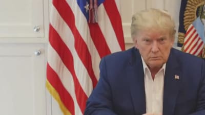Yhdysvaltain presidentti Donald Trump puhuu sairaalassa pöydän ääressä, ei solmiota, taustalla Yhdysvaltain lippu ja valkoista kaapistoa