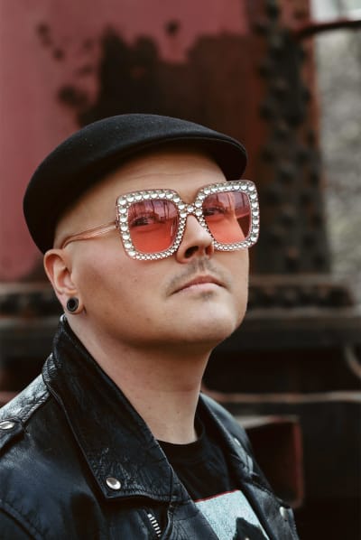 Eino Nurmisto katsoo kameraan vakavalla ilmeellä. Taustalla näkyy punertava vanha tehdaskone.
