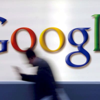 Man med mobil passerar en stor Google-logotyp. 