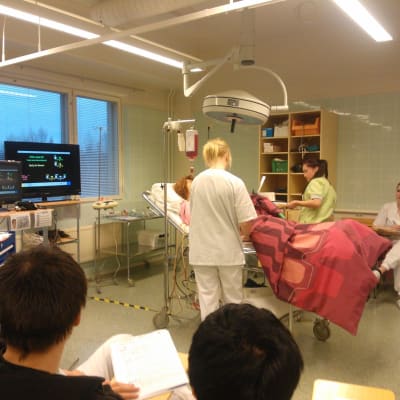 Sjukskötarstuderande på praktisk undervisning med en docka som är kopplad till en hjärtmonitor.