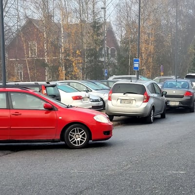 Många parkerade bilar längs en väg. 