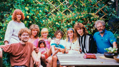 Ett familjeporträtt i trädgården. Familjen är samlad runt ett trädgårdsbord med en grön häck i bakgrunden.