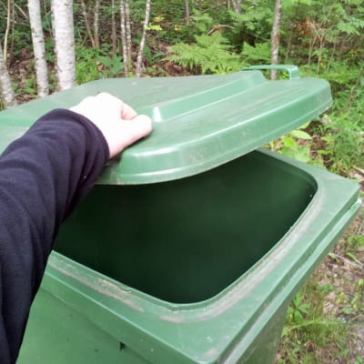 Hand öppnar en grön soptunna av plast