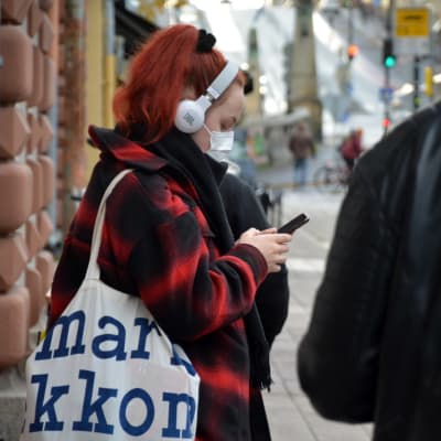 En kvinna kollar i mobilen med munskydd på, på auragatan i Åbo.