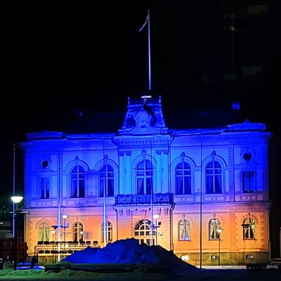Raatihuonen valaistu keltaisella ja sinisellä värillä.
