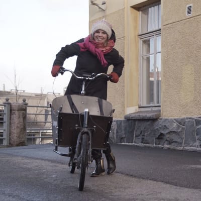 Linda Sundberg med cykel och halsduk framför gult stenhus.