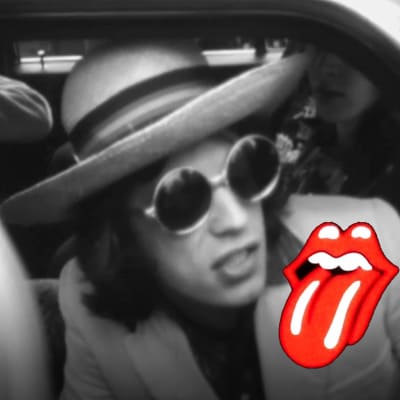 Mick Jagger sitter i bil och intervjuas 1970 i Finland. Svartvit bild med röd Rolling Stones logo på Micks vita kavaj.