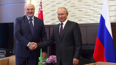 Aleksandr Lukasjenko och Vladimir Putin skakar hand medan de tittar in i kameran.