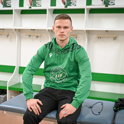 En man sitter på en bänk klädd i fotbollslaget EIF:s gröna tröja. Han heter Tobias Fagerström.