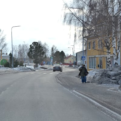 Vöråvägen genom centrala Vörå, fotot taget under en vinterdag i slutet av februari. Vägen är bar men längs sidorna finns snödrivor. En person går på trottoaren. Längre fram syns en bil på vägen.