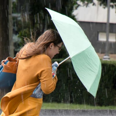 En kvinna i klänning går ute i regnet med ett paraply.
