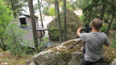 Fotografen Mikko tar bilder på en stugan uppifrån ett berg