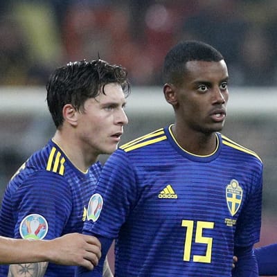 Svenska och rumänska fotbollsspelare följer efter domaren som pekar åt sidan.