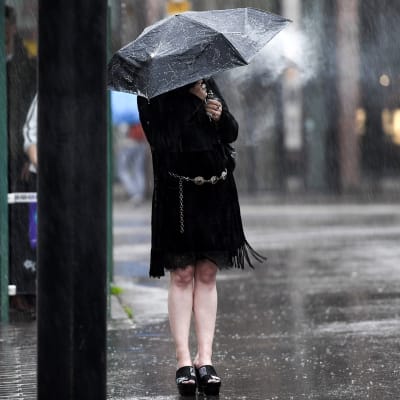 Nainen polttaa sähkötupakkaa sateenvarjon alla sateessa Helsingissä