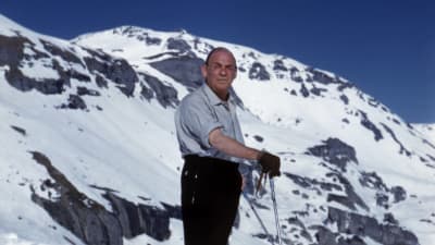 Alvar Aalto poserar med skidorna med snöklädda berg i bakgrunden.