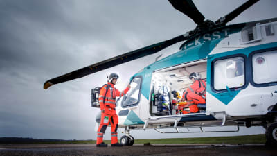 En läkarhelikopter på landningsplatta. En person sitter i helikoptern, en står bredvid